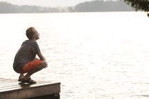 Teenager sitting on dock and praying with head looking up