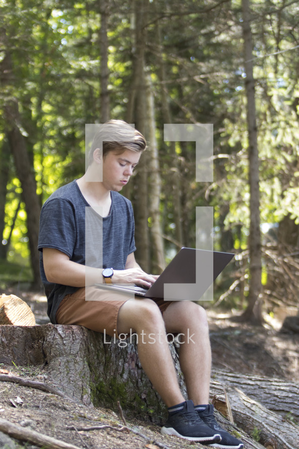Teenager working on laptop computer in rural wooded environment in woods