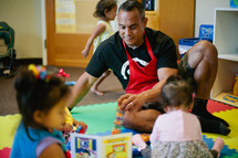 father playing with his toddler daughters in a playroom