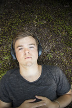 Teenager listening to music and lying down on grass and earthy background looking at camera