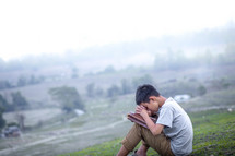 a boy sitting on a hill praying 