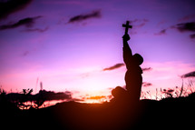 silhouette of a cross and a boy praying outdoors at sunset 