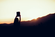silhouette of a girl holding up a Bible 