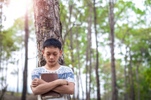 a teen boy praying in a forest 