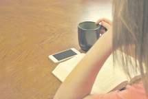 woman reading a Bible with a coffee mug, and cellphone on the table 