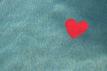a red paper heart floating on turquoise water 