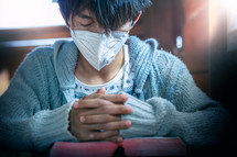 a woman in a face mask praying over a Bible 