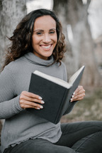 A smiling young woman reading a book 
