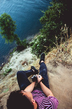 a man with a camera sitting at the edge of a cliff 