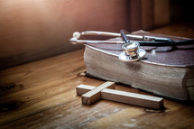 stethoscope, cross, and Bible on a wood table 