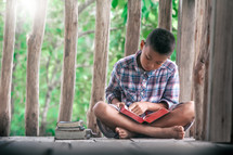 a boy reading a Bible outdoors on a deck 