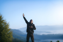 a man in a coat standing on a mountaintop praying 