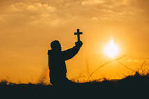 a boy holding a cross at sunset 