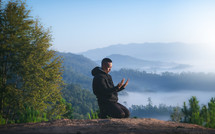 a man kneeling in prayer on a mountaintop 