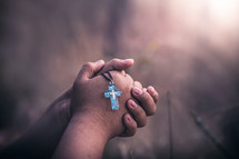 praying hands holding a cross necklace 