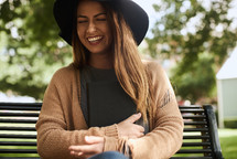 a woman laughing sitting on a park bench 