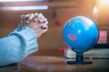 praying hands near a globe 