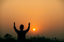 silhouette with raised hands at sunset 