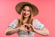 Smiling pretty woman showing sign of shape heart. Positive lady on pink background. Women health, volunteering, charity donation, gratitude symbol, flirting concept. High quality 