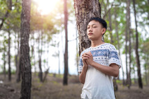 a teenage boy praying in a forest 