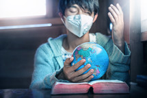 person wearing a face mask with praying hands on a globe 
