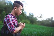 Young farmer sitting praying in a corn field