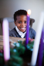 A smiling African American boy behind an Advent wreath 