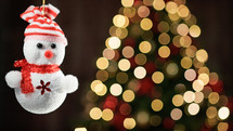 Tiny snowman decoration with Christmas tree in the background