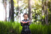 a little girl reading a Bible alone in a forest 