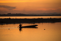 Silhouette of a man with an oar in a boat on the lake water at sunset.