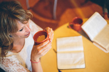 Woman drinking a cup of coffee, an open bible on the table in front of her