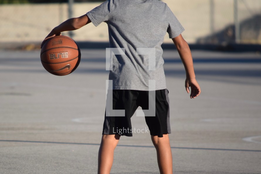 an African American boy dribbling a basketball outdoors 