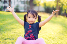 a little girl with open arms sitting in grass 