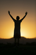 teen boy standing in warm sunlight with arms raised 