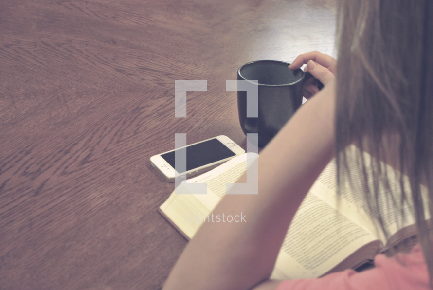 woman reading a Bible, coffee mug and cellphone 