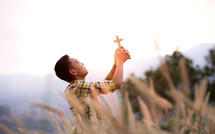 a young man holding a cross praying in a field 