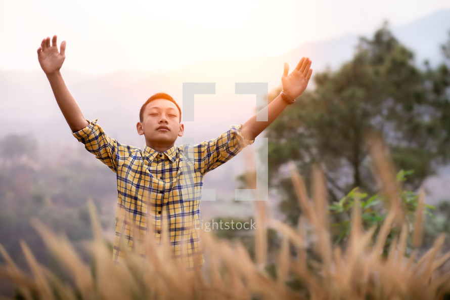 a young man in a field with hands raised 