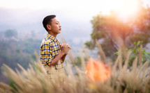 a young man standing in a field praying 