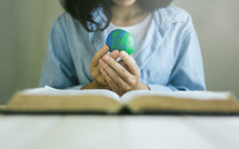 a woman holding a globe over the pages of a Bible 