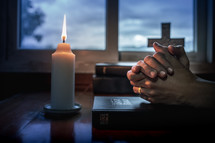 Bible with candlelight and praying hands