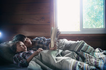 a sick child lying in bed reading a Bible with mom 