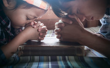 father and daughter praying over a Bible 