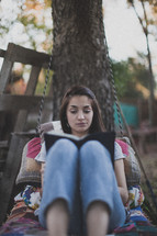 A young woman sitting on a swing and reading the Bible