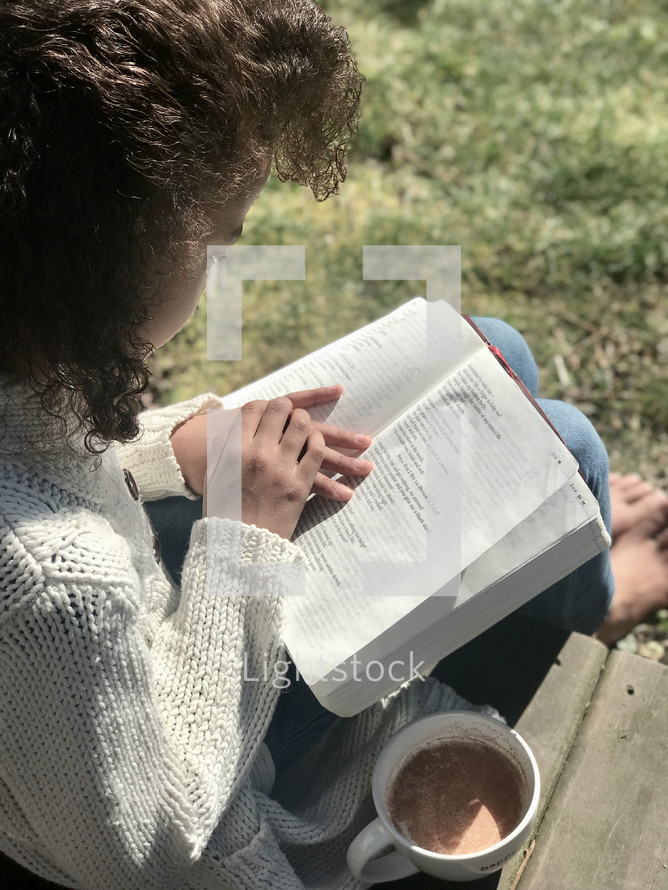 a woman reading a Bible in her lap outdoors 