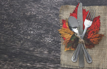 burlap placemat and silverware on fall leaves for dinner party 