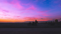 a man with a bike resting on the side of a road at sunset 