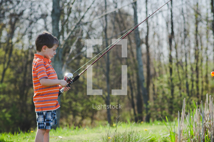 A boy holding a fishing pole at a pond on a sunny summer day.