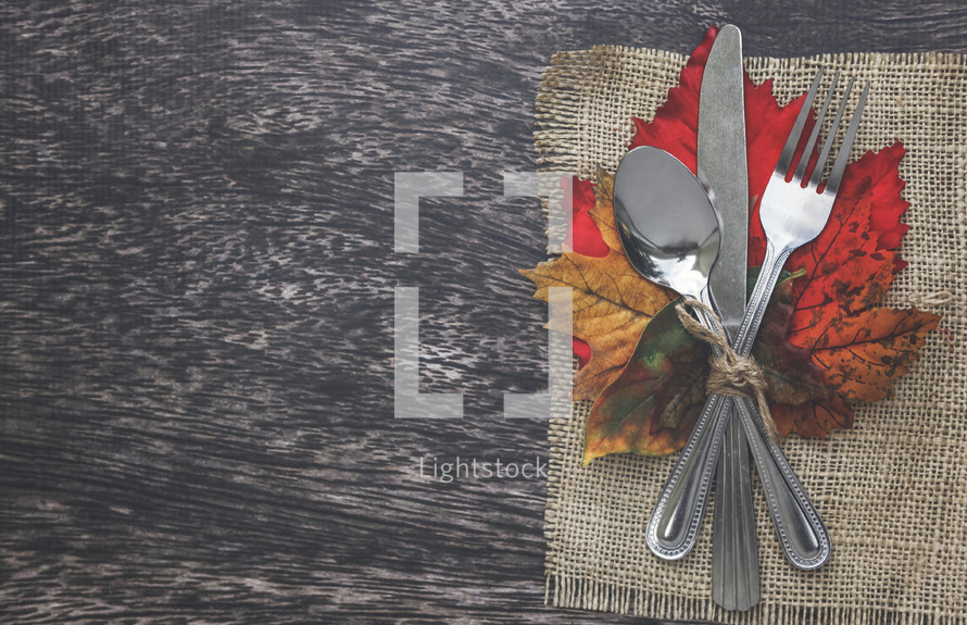 burlap placemat and silverware on fall leaves for dinner party 