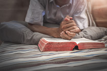 a man praying over a Bible in bed 