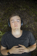 Teenager listening to music and lying down on grass and earthy background